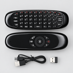 Black remote control with keyboard layout and additional buttons, accompanied by a USB cable and adapter on a wooden surface.
